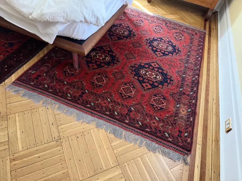 A red geometric rug beside a bed on a parquet floor