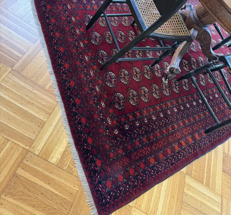 A red patterned rug under a dining chair on a parquet floor