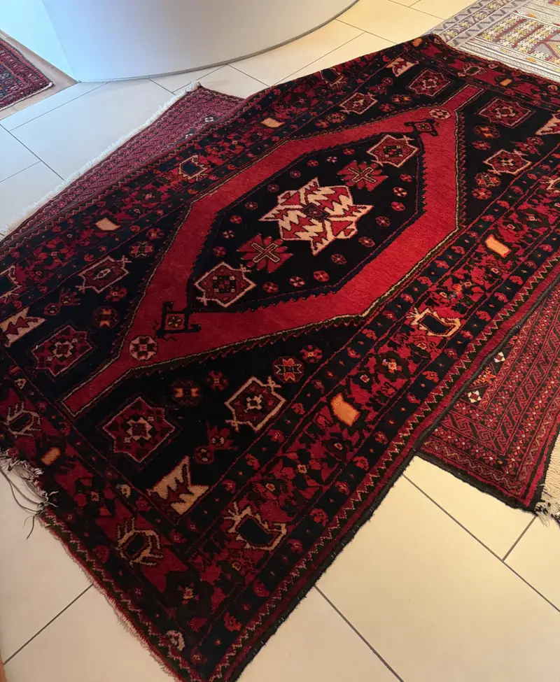 Two red tribal rugs on a white tile floor