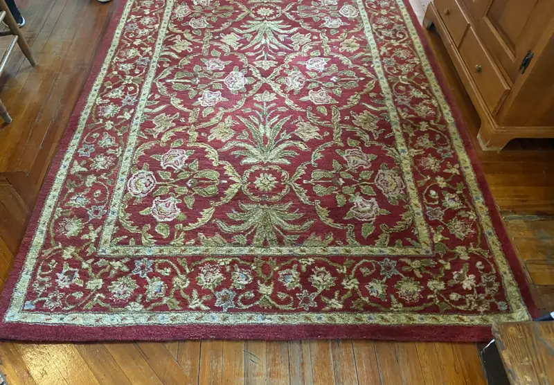 A red floral rug with a green border on a wood floor