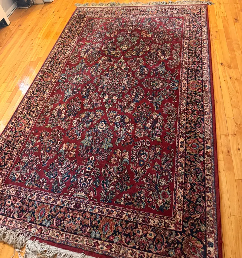 A red rug with a dense floral pattern on a wood floor